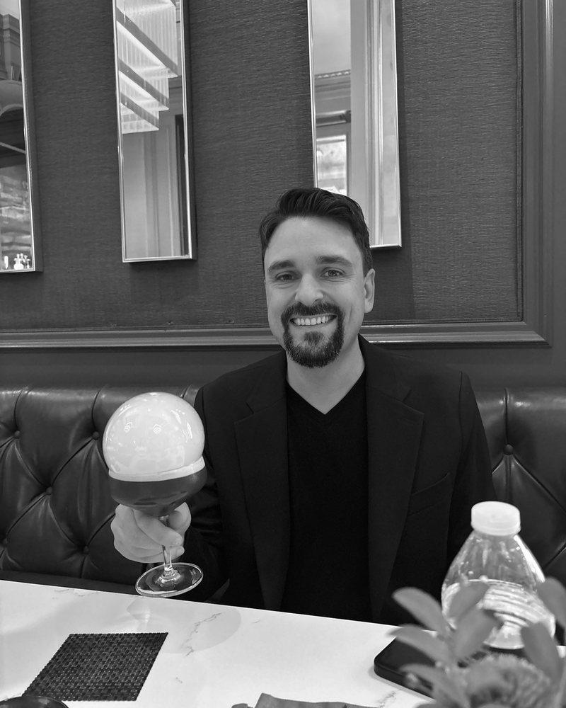Black-and-white portrait of Caleb Leak, Momo's Chief of Staff, in a dark jacket.